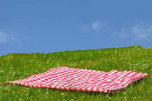 Red picnic cloth. Red checked picnic blanket on a meadow with daisies in bloom and cloudy sky. Beautiful backdrop for your product placement or montage.