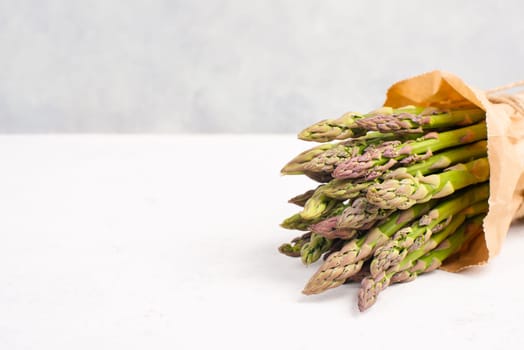 Fresh green bundle of asparagus on a white textured table, vegetables in spring, gourmet cuisine food, cooking a vegan meal