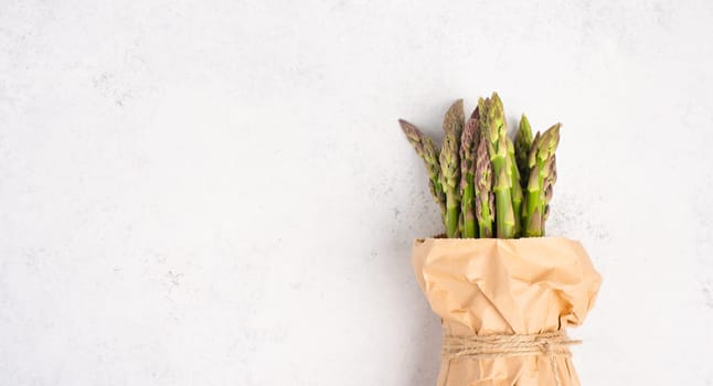 Fresh green bundle of asparagus on a white textured table, vegetables in spring, gourmet cuisine food, cooking a vegan meal