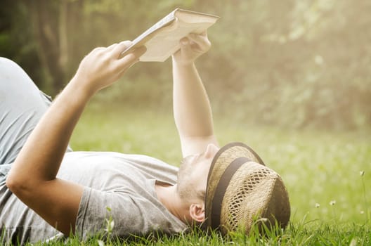 Young man lying in the grass, relaxing and reading a book. Retro filter