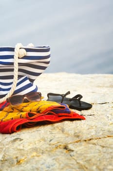 Sunglasses, towel, bag and flip-flops on the beach. Summer holiday concept.