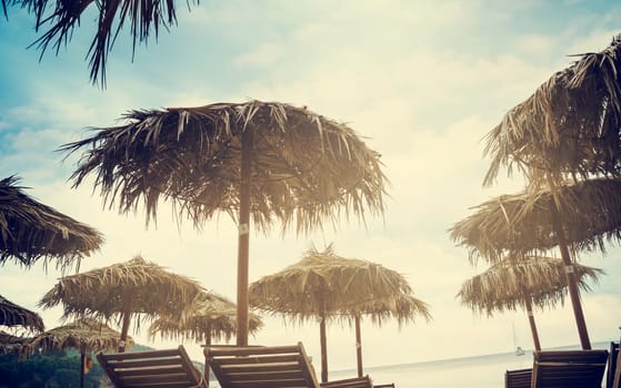 Straw Parasols at the tropical sandy beach. Retro filter.