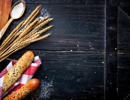 Bread, wheat ears and flour on rustic black table.