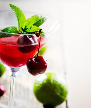 Iced cherry cocktail in martini glass with lime on wooden table.