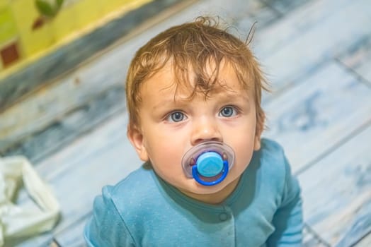 white baby boy with blue eyes with a pacifier in his mouth looks up