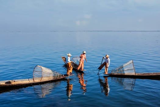 Myanmar travel attraction landmark - three traditional Burmese fishermen with fishing nets on boats at Inle lake