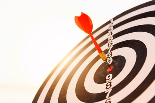 Dart arrow hit to center on bullseye(bull's-eye) of a dartboard is a target of purpose challenge business at sunset, expert strategy market target, objective financial and goal a concept