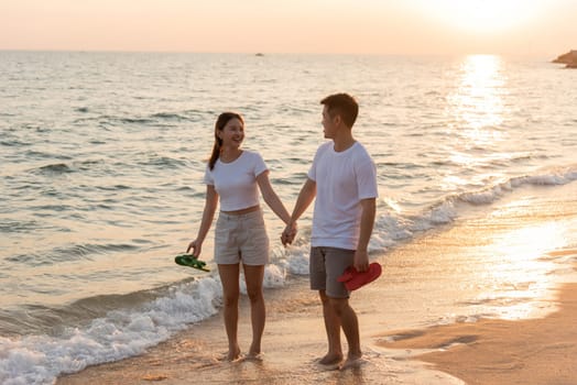 Vacation loving couple walking on beach together at sunset landscape, relaxing vacation travel summer, Asian man and woman in love holding hands walks along the sandy seashore