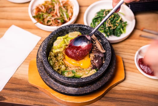 Bibimbap in a black heated stone bowl, Korean traditional dish- bibimbap mixed rice with vegetables Include beef and fried egg, Japanese hot pot food