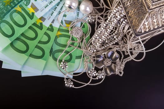 Silver jewelry and euro on black background.