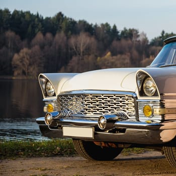 Old retro or vintage car or automobile front side with front lights or headlights and radiator grill on the lake