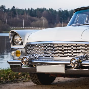 Old retro or vintage car or automobile front side with front lights or headlights and radiator grill on the lake