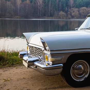 Old retro or vintage car or automobile front side with front lights or headlights and radiator grill on the lake