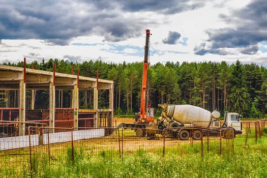 Building under construction at a construction site with crane and concrete mixer. Processed by hdr effect filter
