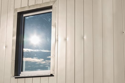 Window with sun reflection in light yellow color plastic siding panels wall