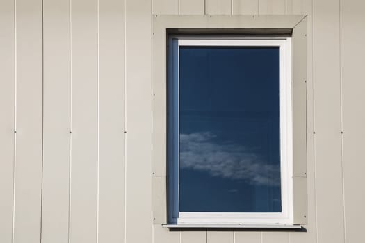 Window with sky reflection in light yellow color plastic siding panels wall