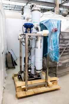 Unpacked equipment on pallets in interior of industrial building under construction on pharmaceutical industry manufacture or chemical plant
