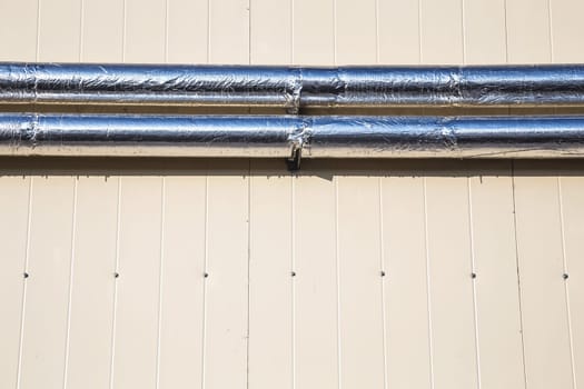 Metal chrome pipes on yellow plastic siding wall