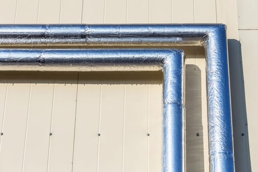 Metal chrome pipes on yellow plastic siding wall