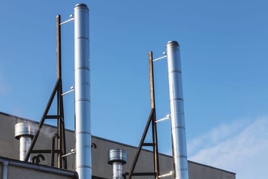 Smoke metal pipes on rooftop of industrial building against blue sky background