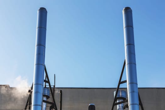 Smoke metal pipes on rooftop of industrial building against blue sky background