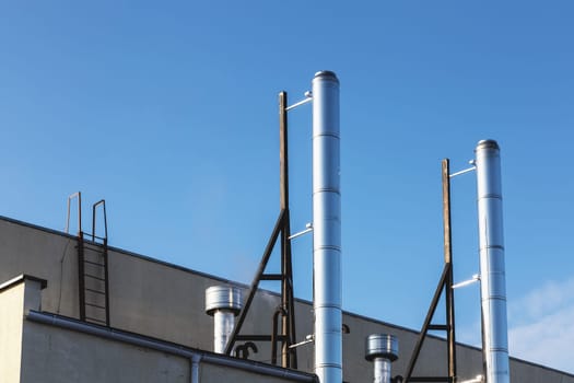 Smoke metal pipes on rooftop of industrial building against blue sky background