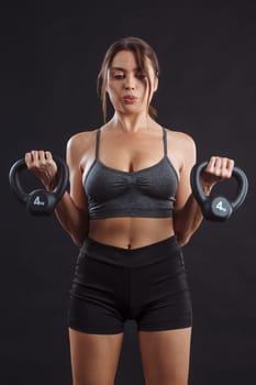 Young sexy woman exercising and doing bicep curls with a kettle bells.