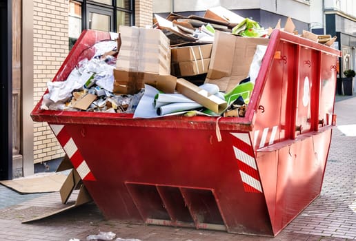 Red metallic Container filled with cardboard Trash in front of a shop downtown