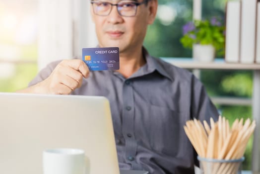 Closeup Asian senior adult man holding credit card and using technology on laptop computer, Online shopping payment with a customer network connection via an Omnichannel system
