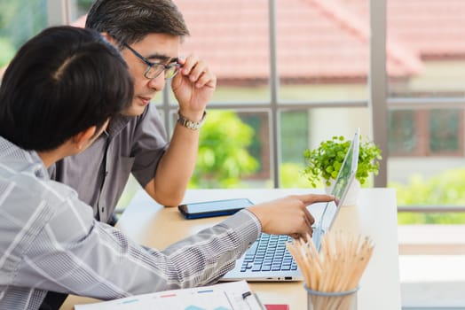 Asian young man teaching senior father how to use a modern laptop computer together in the living room at home, Son helping Dad to use the laptop for web application online