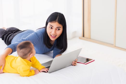 Asian new young beautiful mother finding and reads information on a laptop for milk mixing on a bottle in the bedroom at home
