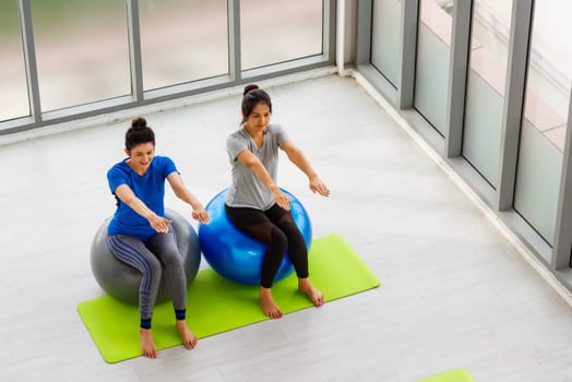 Above two Asian adult and young woman in sportswear doing aerobics yoga exercise with sitting on fitness ball indoor yoga studio, fit sport healthy workout lifestyle exercise