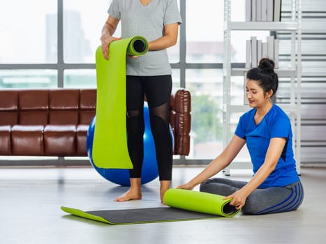 Asian adult and young woman smiling holding a yoga mat after yoga and exercise. Portrait of happy beautiful female standing hold yoga mat indoor studio, sport healthy workout concept