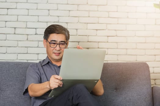 Asian lifestyle senior man with eyeglasses reading news on laptop, Old businessman having video call on laptop computer at home office talk using modern technologies and wireless connection