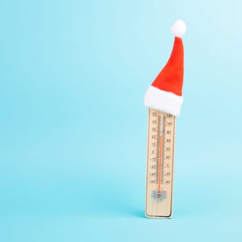 Thermomter with a cute red christmas hat, blue background, copy space for text, greeting card for holiday, winter season