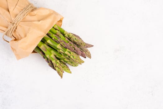 Fresh green bundle of asparagus on a white textured table, vegetables in spring, gourmet cuisine food, cooking a vegan meal
