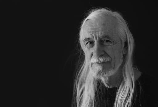 Low key studio black and white portrait of smiling attractive old man with loose long gray hair. Horizontally.