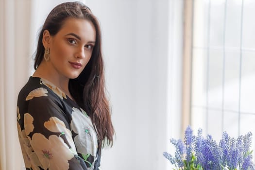 Attractive dark haired girl is posing next to purple flowers. Horizontally.
