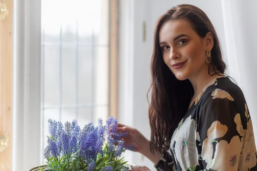 Attractive dark haired girl is holding  purple flowers in a pot. Horizontally.