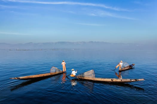 Myanmar travel attraction landmark - Traditional Burmese fishermen with fishing nets on boats at Inle lake in Myanmar famous for their distinctive one legged rowing style