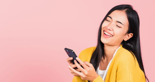 Happy Asian portrait beautiful cute young woman excited laughing holding mobile phone, studio shot isolated on pink background, female using funny smartphone making winner gesture