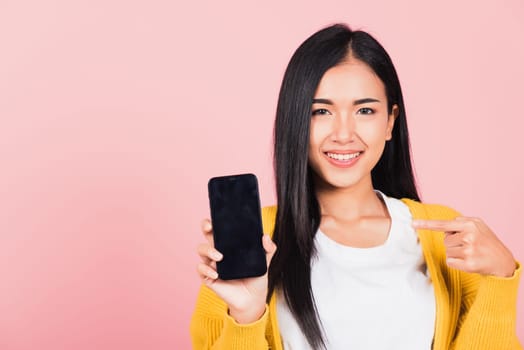 Portrait Asian happy beautiful young woman smile making finger pointing on smartphone in hand shopping online application looking to camera isolated, studio shot pink background with copy space