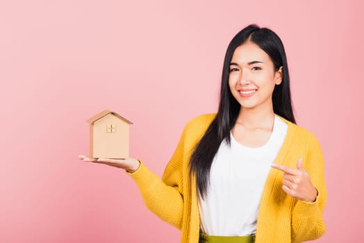 Happy Asian portrait beautiful cute young woman excited smiling holding house model on hand, studio shot isolated on pink background, broker female hold home real estate insurance and banking concept