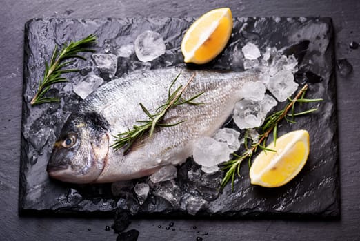 Seafood cooking preparation.Top view of dorado and shrimps with herbs and lemon on black slate.