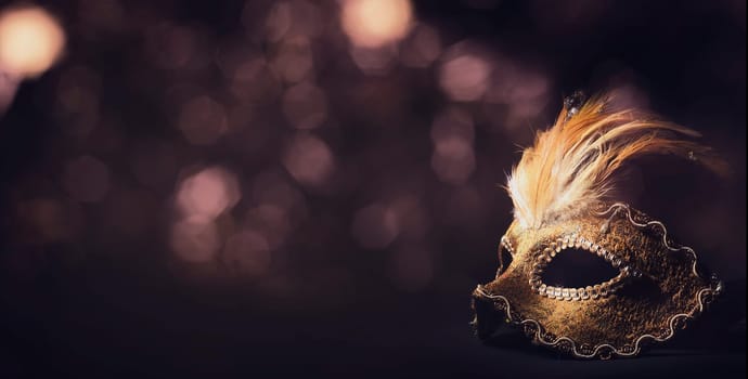 Golden venetian ball mask in front of the night bokeh lights. Masquerade party or holiday event celebration concept.