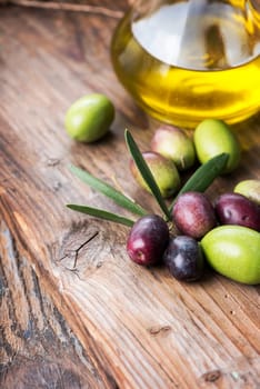 Fresh olives and extra virgin olive oil bottle on wooden textured board.