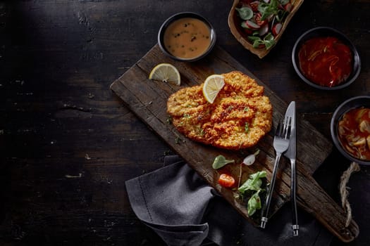 Top view of tasty schnitzel with fresh lemon slices against radish and spinach salad on brown background