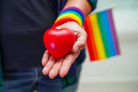 Asian woman holding red hert with rainbow flag, LGBT symbol rights and gender equality, LGBT Pride Month in June.