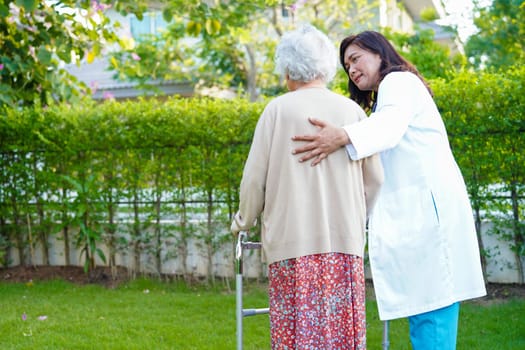 Doctor help Asian elderly woman disability patient walk with walker in park, medical concept.