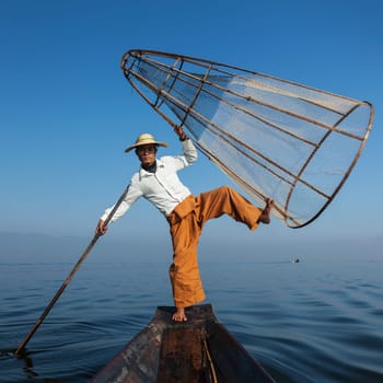 Myanmar travel attraction landmark - Traditional Burmese fisherman with fishing net at Inle lake in Myanmar famous for their distinctive one legged rowing style
